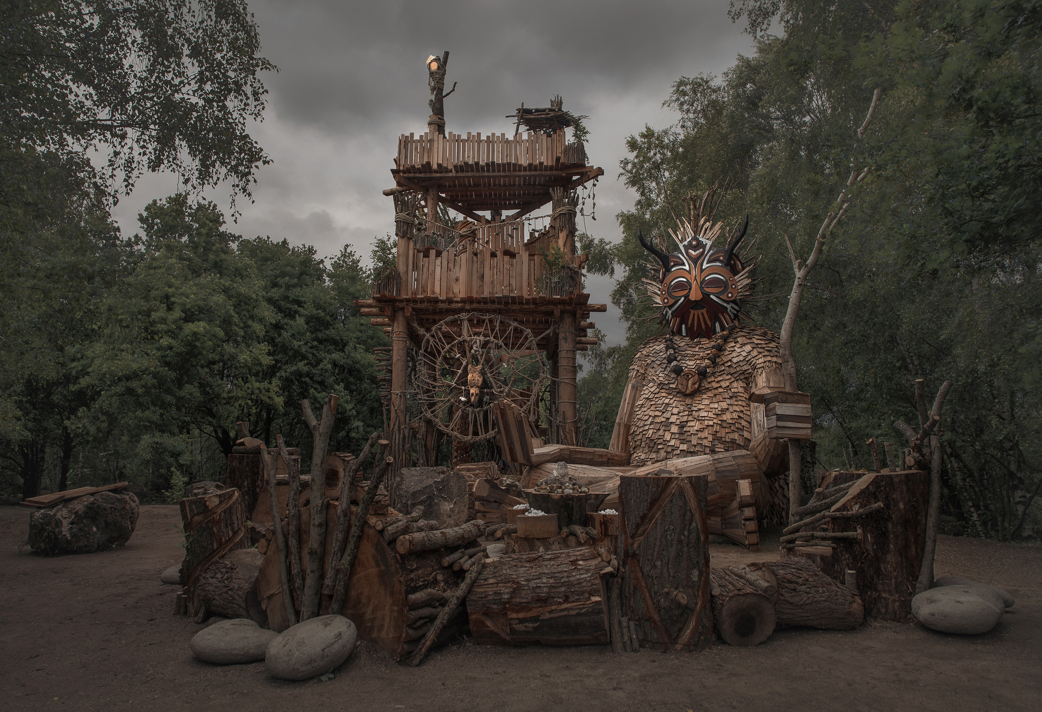 The 7 trolls are from 18 to 7 meter long. The tower is 17 meters tall. It took Dambo and a crew of 15 people around 25 weeks to build it. The wood is mainly old shelves from a supermarket, pallets, and branches from fallen trees. It is located in a Belgian forest.