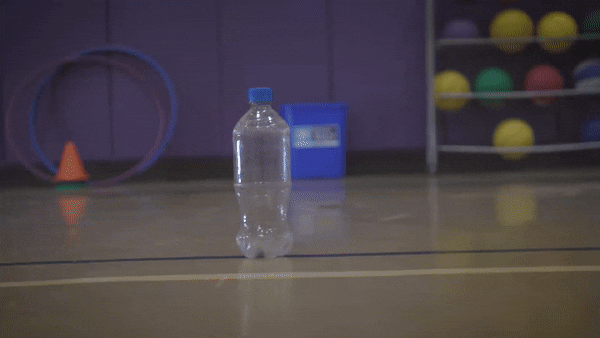 A student favorite. Try standing about a step behind the bottle at about a 45° angle. Be sure to point your toe and kick through with your stronger foot. Understand that the kicking part is easy, but aiming is a bit more challenging. You want to kick the bottom of the bottle. As you kick, make sure the laces of your shoe are aimed at the recycling bin. This will make your kicks more accurate.