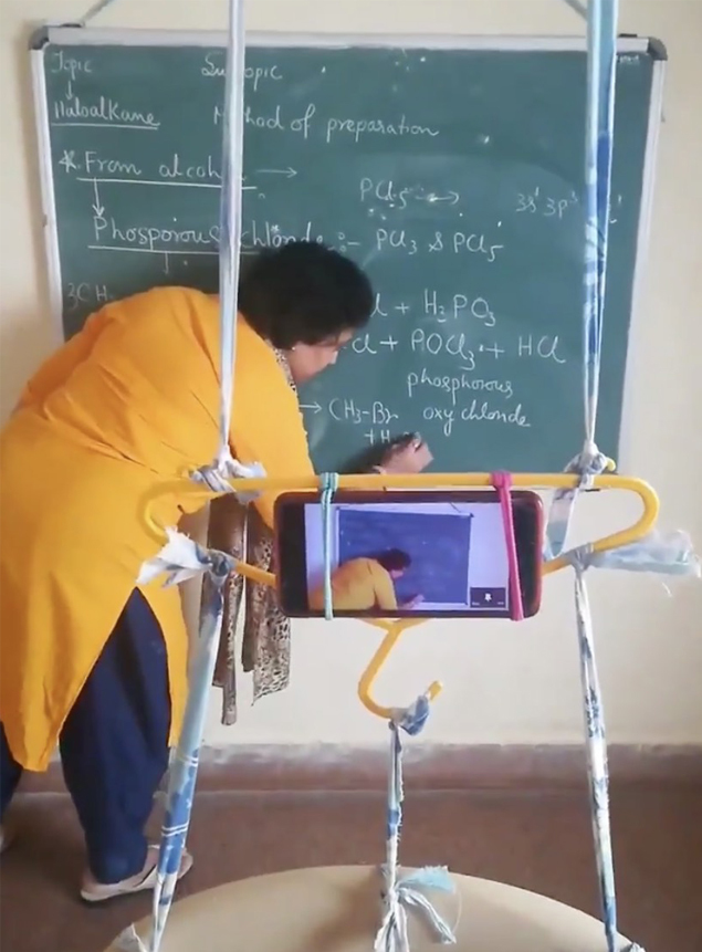 To ensure that her students could see the chalkboard, the teacher - who did not have a tripod - came up with a jugaad or hack. She tied her phone to a clothes hanger and suspended it between a plastic chair and the ceiling to create a makeshift tripod, allowing her students to look at the chalkboard as she taught.  
