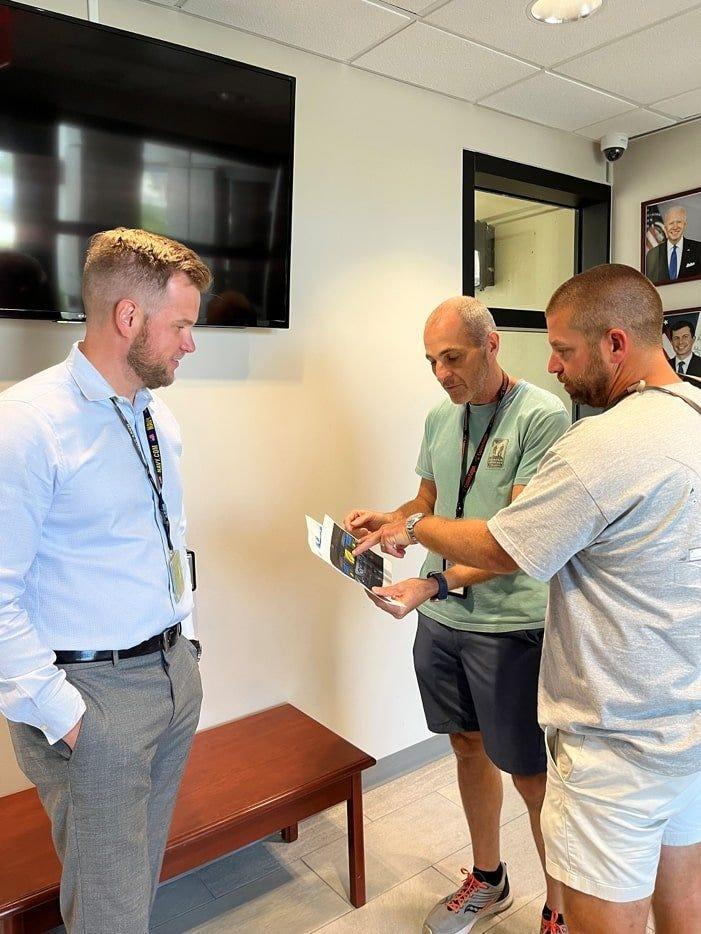Air Traffic Manager Ryan Warren (left) and controller Robert Morgan (center) show the passenger Darren Harrison (far right) print outs of the Cessna 208 flight deck they used to help him land safely at Palm Beach Airport after an in-flight emergency on May 10, 2022.