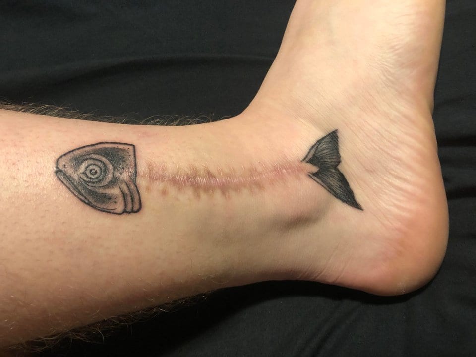 Aquí hay otro tatuaje de un pez que incorpora la cicatriz como parte del diseño. El patrón de puntada incluso se parece a las espinas de pescado. Aunque no es tan activo como el anterior tatuaje de marlín, creo que este tatuaje cumple con su función igual de bien.