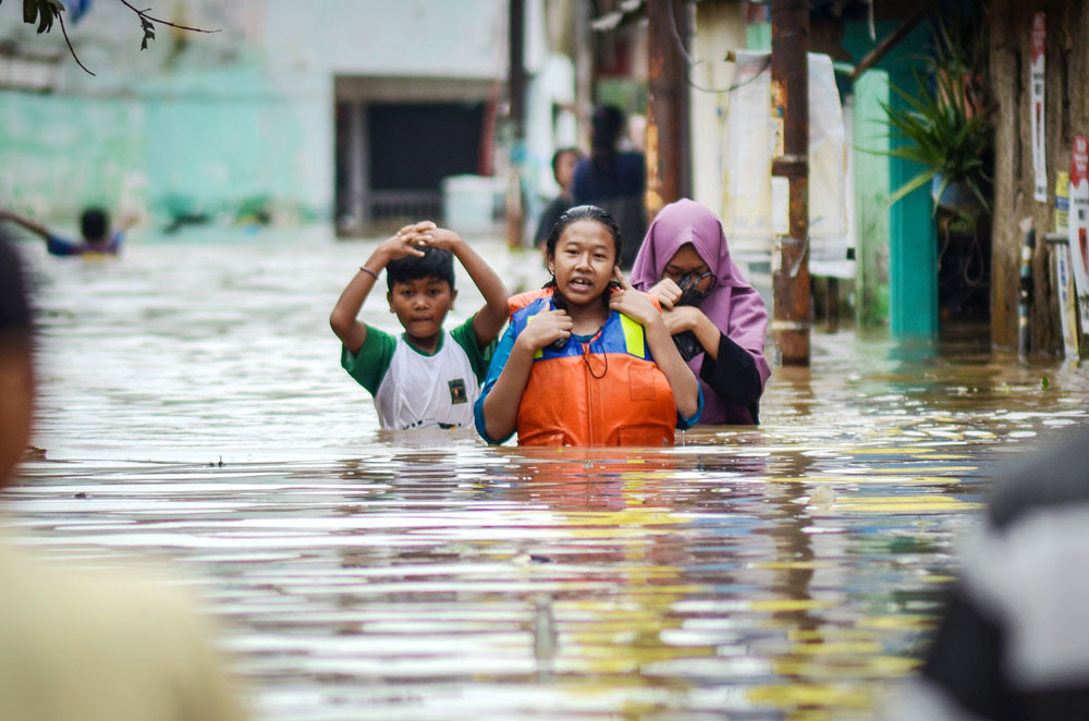 Residents wade across an inundated road in Dayeuhkolot, Bandung regency, West Java on Jan. 14. Heavy rain caused the Citarum River to overflow and flood several areas with water rising to between 60 and 150 centimeters high.