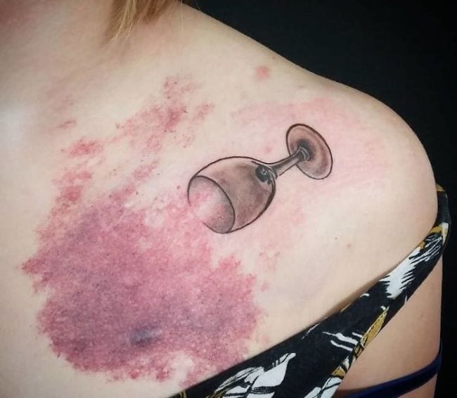 This tattoo takes a large birthmark and makes it a part of the tattoo. Notice how the birthmark looks almost like an area of spilled wine. So, the addition of the wine glass makes it seem like a natural part of the overall tattoo.